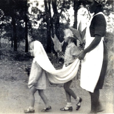 Image from the collection titled "Lady in Waiting" from the 1930s-1940s.  Its shows two children and their nanny walking.  The youngest child is walking in front with a cloth on her head and the nanny carrying the end like a wedding veil.